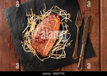 Carne di Kobe, wagyu beef steak, cotta con di germogli di fagioli di soia, overhead shot su un nero ardesia piastra Foto Stock