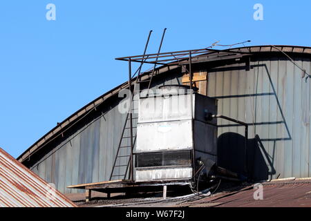 Rotto fatiscenti di metallo grande uscita di ventilazione montata con arrugginita gabbia metallica sulla parte superiore delle industriale abbandonato edificio complesso Foto Stock