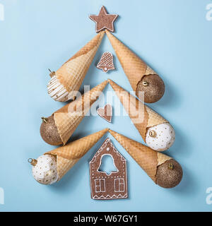 Albero di Natale fatto di coni gelato festosa e palle di Natale con biscotti allo zenzero su un brillante sfondo blu. Vista superiore, laici piatta Foto Stock