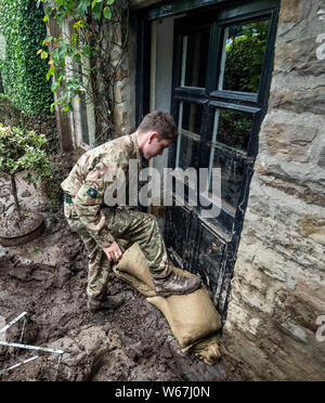 Un soldato da 2 Yorks Stack i sacchi di sabbia in Grinton, North Yorkshire dopo che parti della regione avevano fino a 82.2mm di pioggia in 24 ore il martedì. Foto Stock