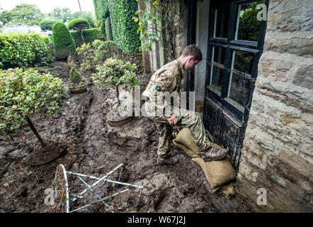 Un soldato da 2 Yorks Stack i sacchi di sabbia in Grinton, North Yorkshire dopo che parti della regione avevano fino a 82.2mm di pioggia in 24 ore il martedì. Foto Stock