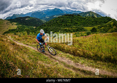 MORZINE, Francia. Un mountain biker in sella a una singola traccia di sentiero sebbene prateria alpina con drammatica nuvole e ripide montagne in distanza. Foto Stock