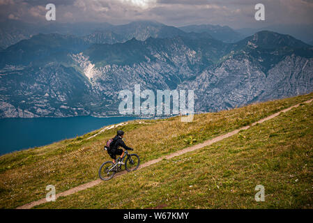 Il LAGO DI GARDA, Italia. Un mountain biker in sella ad un buon single-track trail sebbene pascolo verde in alto sopra il Lago di Garda con sensazionali montagne e nuvole mi Foto Stock