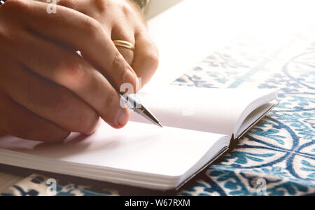 Maschio di mani tenendo la punta di una penna a sfera per scrivere sulle pagine vuote di un quaderno. Momento creativo. Ispirazione.