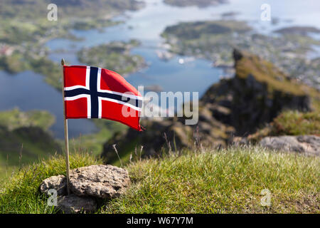 Bandiera norvegese sulla montagna Nonstinden. Sfocati sullo sfondo la visualizza in basso a Ballstad, Vestvågøya isola, isole Lofoten in Norvegia Foto Stock