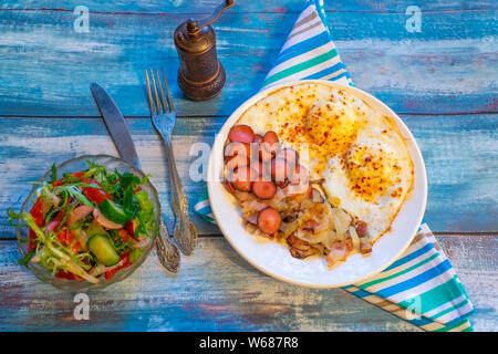 Uova strapazzate con pancetta, cipolla e salsiccia. Su di un piatto sul tavolo. Foto Stock