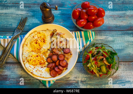 Uova strapazzate con pancetta, cipolla e salsiccia. Su di un piatto sul tavolo. Foto Stock