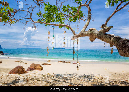 Vuoto spiaggia da sogno con sabbia bianca dell'isola di Koh Ngai, Thailandia. Gusci appeso a un ramo di albero su una stringa. Foto Stock