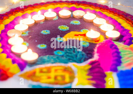 Bella rangoli realizzato da polveri colorate e decorate con candele di cera diyas il Diwali eve. Questi modelli sono realizzati a mano da indù e decorare Foto Stock