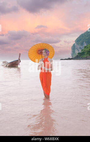 Un Felice attraente Medioevo turista femminile in un sarong con un ombrello Thi e fiori nei capelli in Phang-nga Bay in isole di Phi Phi Thailandia. Foto Stock