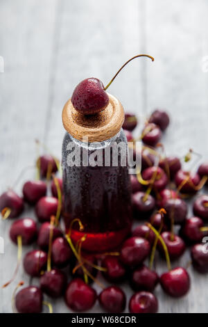 Drink di ciliegia della bottiglia con ciliegie fresche bacche su sfondo di legno. Vista dall'alto. Foto Stock