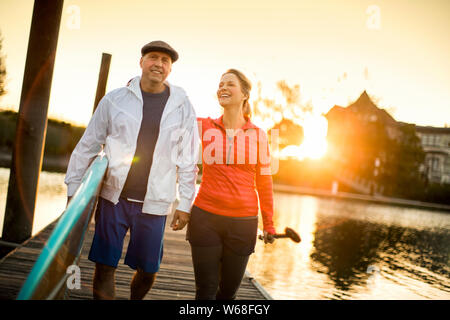 Felice paddleboarding giovane a piedi lungo un molo al tramonto. Foto Stock