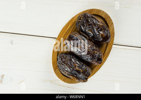 Gruppo di tre essiccato intero data marrone medjool sulla piastra di bambù flatlay su legno bianco Foto Stock