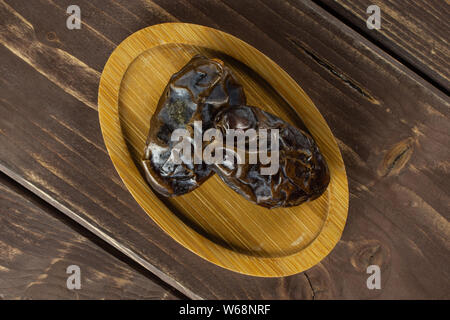 Gruppo di due interi essiccati marrone medjool data sulla piastra di bambù flatlay su legno marrone Foto Stock