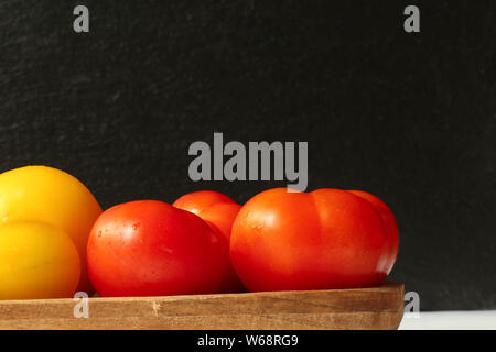 Rote Tomaten auf Holzbrett auf schwarzem Schiefer Hintergrund Foto Stock