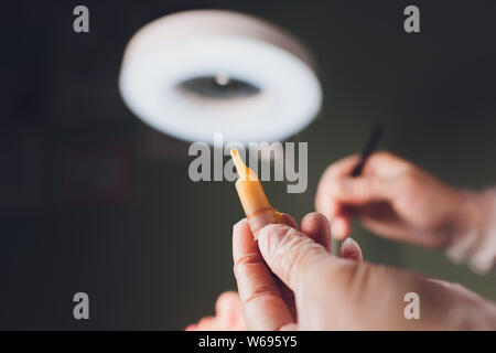 Le mani di una donna bella caduta collagene Siero idratante della faccia in chiaro flacone giallo luce morbida dello sfondo. Protettore della pelle del viso Trattamento Foto Stock