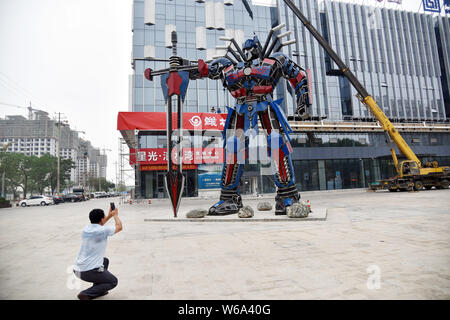 Un uomo cinese prende le immagini di una replica di Optimus Prime fatta di scarti di automobile di fronte a un complesso commerciale in Liaocheng city east mento Foto Stock