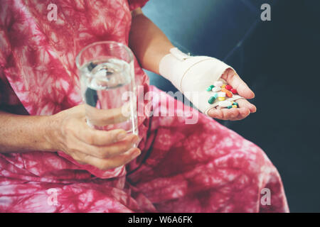 Senior donna asiatica prendere la pillola medicina a portata di mano mentre è seduto sul divano di casa Foto Stock