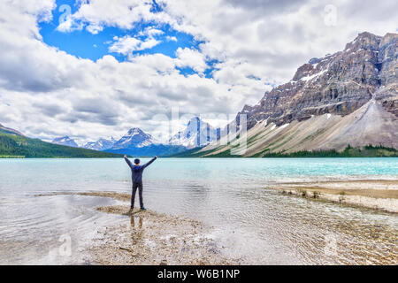 Uomo con braccia alzate di fronte al Lago Bow nel Parco Nazionale di Banff, con montagna Crowfoot e il Ghiacciaio Crowfoot in background. Foto Stock