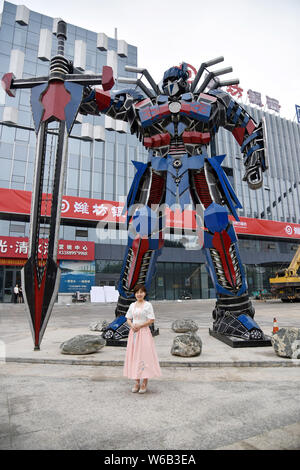 Una donna cinese pone per le foto con una replica di Optimus Prime fatta di scarti di automobile di fronte a un complesso commerciale in Liaocheng city, EAS Foto Stock