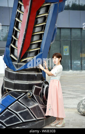 Una donna cinese pone per le foto con una replica di Optimus Prime fatta di scarti di automobile di fronte a un complesso commerciale in Liaocheng city, EAS Foto Stock