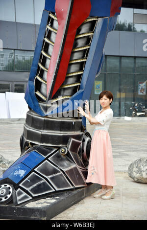 Una donna cinese pone per le foto con una replica di Optimus Prime fatta di scarti di automobile di fronte a un complesso commerciale in Liaocheng city, EAS Foto Stock