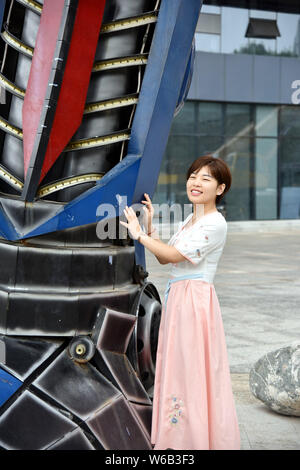 Una donna cinese pone per le foto con una replica di Optimus Prime fatta di scarti di automobile di fronte a un complesso commerciale in Liaocheng city, EAS Foto Stock