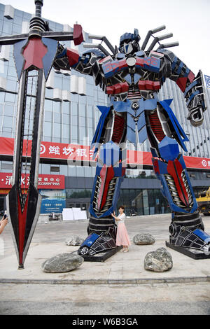 Una donna cinese pone per le foto con una replica di Optimus Prime fatta di scarti di automobile di fronte a un complesso commerciale in Liaocheng city, EAS Foto Stock