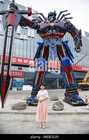 Una donna cinese pone per le foto con una replica di Optimus Prime fatta di scarti di automobile di fronte a un complesso commerciale in Liaocheng city, EAS Foto Stock