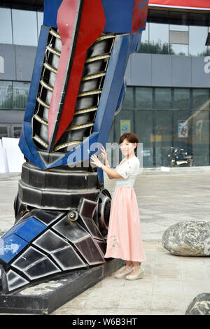 Una donna cinese pone per le foto con una replica di Optimus Prime fatta di scarti di automobile di fronte a un complesso commerciale in Liaocheng city, EAS Foto Stock