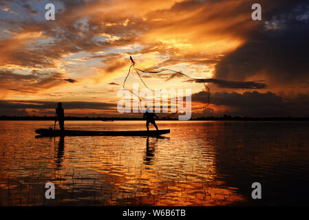 Asia fisherman net utilizzando sulla barca di legno netto di colata il tramonto o l'alba nel fiume Mekong - Silhouette fisherman barca con sfondo di montagna la vita pe Foto Stock