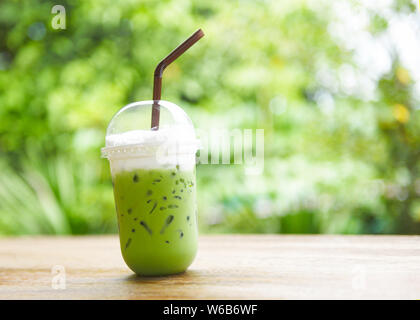Iced tè verde in una tazza di plastica / tè verde Matcha latte frappé e paglia sul tavolo di legno con lo sfondo della natura Foto Stock