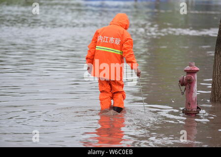 Un lavoratore cinese sgombra di fango e foglie su una strada allagata causato dalla pioggia pesante nel distretto di Dongxing, Neijiang city, a sud-ovest della Cina di Sichuan prov Foto Stock