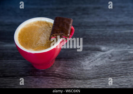 Espresso in casa piatto bianco nel colore rosso brillante cup in legno scuro dello sfondo. Perfetto con un biscotto di cioccolato. Sensazioni di calore, lusso, ricompensa. Il contrasto Foto Stock