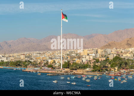 Aqaba Giordania - 6 Novembre 2017: Cityscape di Aqaba e Bandiera della Giordania sventolare sopra la città. Bandiera araba di Revolt-Sixth più alto pennone nel mondo Foto Stock
