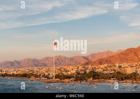 Aqaba Giordania - 6 Novembre 2017: Bandiera della Giordania sventolare sopra la città al tramonto. Bandiera araba di Revolt-Sixth più alto pennone del mondo. Foto Stock