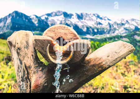 Acqua fresca di sorgente di acqua che gocciolava con la gamma della montagna sullo sfondo Foto Stock