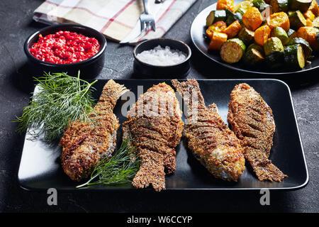 Appena panate carassio carpe nero a piastra rettangolare su una tabella di calcestruzzo con zucchine fritte e salsa di pomodoro caldissima, vista orizzontale da ab Foto Stock