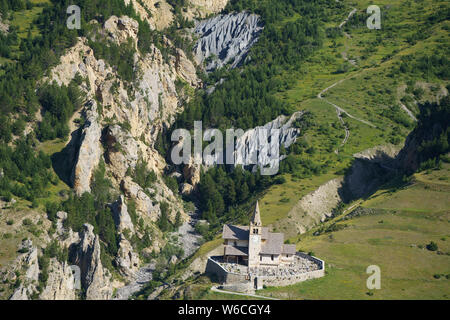 VISTA AEREA. Chiesa remota di Saint-Michel e cimitero con un pittoresco canyon per sfondo. Cervières, Hautes-Alpes, Francia. Foto Stock