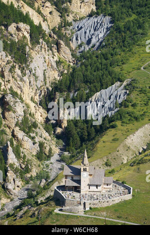 VISTA AEREA. Chiesa remota di Saint-Michel e cimitero con un pittoresco canyon per sfondo. Cervières, Hautes-Alpes, Francia. Foto Stock