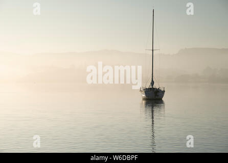 Bellissimo paesaggio unplugged immagine di yacht a vela seduto ancora nel lago calmo acqua nel distretto del lago durante la pacifica misty Autumn Fall sunrise Foto Stock