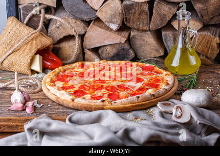 Pizza con salsiccia e pepe bulgaro vicino alla legna da ardere Foto Stock