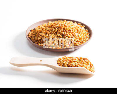 Fenugreek (Trigonetla) su una piastra di argilla con un cucchiaio di legno in primo piano su uno sfondo bianco Foto Stock