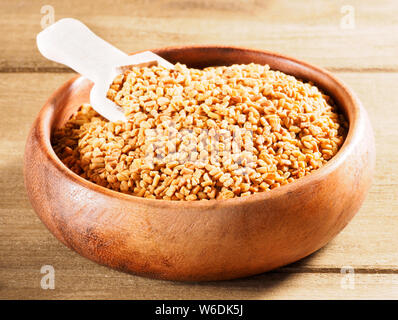 Fenugreek (Trigonella) in una coppa di legno con scoop su uno sfondo di legno Foto Stock