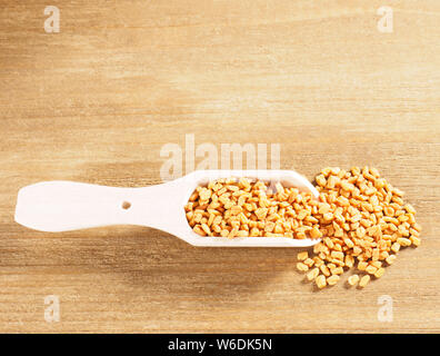 Fenugreek (Trigonella) in un cucchiaio di legno su un sfondo di legno Foto Stock