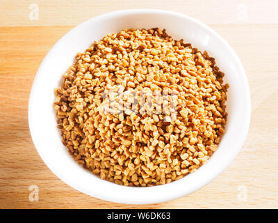 Fenugreek (Trigonella) in bianco coppa in ceramica su un sfondo di legno Foto Stock