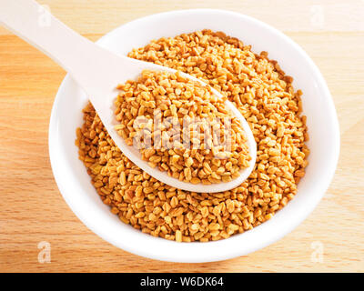 Fenugreek (Trigonella) in tazza bianca su un cucchiaio di legno su un sfondo di legno Foto Stock