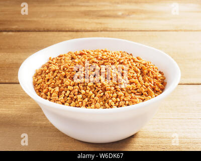 Fenugreek (Trigonella) in un bianco coppa in ceramica su uno sfondo di legno Foto Stock