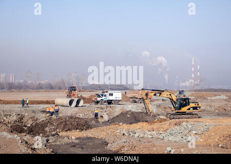 Escavatore foratura sul campo di massa alla infrastruttura di fondazione cantiere, i lavoratori professionali in uniforme e carrello contro la città industriale ba Foto Stock