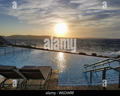 Spettacolare piscina infinity con sdraio in prossimità della costa al tramonto Foto Stock